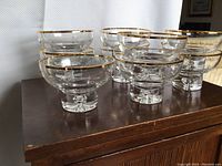 Nine clear glass dessert bowls with gold rims and gold dots arranged on a wooden surface.