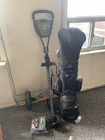 Photo showing golf bag with clubs and the attached push caddy, placed beside a window and carpet floor.