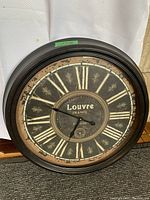 Front facing photo showing the entire clock face with Roman numerals and decorative fleur-de-lis, highlighting the vintage distressed look and frame shape.