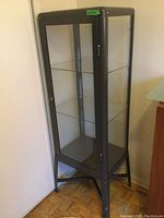 Front, side and top view of metal curio display case showing glass panels and metal frame