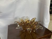 Front view of the vintage Murano glass sculpture placed on a wooden surface, showing its floral, petal-like shape and amber color with clear edges.
