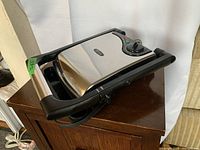 Closed Bella panini press showing stainless steel top, black plastic sides, temperature dial, and indicator lights.