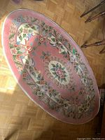 Oval vintage pink floral accent rug with detailed floral border and central rose medallion on hardwood floor.