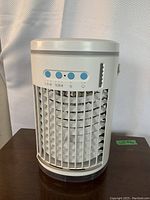 Front view of white cylindrical portable air conditioner with control buttons and vented front grill.