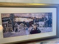 Framed oil painting showing winter village with horse and sleigh, gold frame and beige border visible
