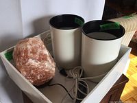 Photo of two white cylindrical vintage desk lamps with black interiors and one large rough pink Himalayan salt lamp on a white surface.