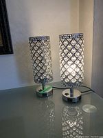 Two crystal bead table lamps on a glass surface, one lamp switched on showing internal light and crystal bead lattice design.