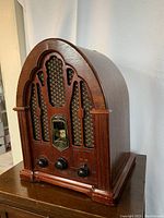 Side-left angled view of the radio showing the curved wooden case, decorative grille, and three control knobs.