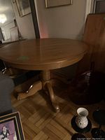 Photos of vintage solid oak round pedestal dining table showing the top surface, base with four curved feet, and general condition around the table's surroundings.