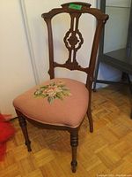 Front angle showing carved wooden backrest and embroidered rose floral design on blush pink seat upholstery.