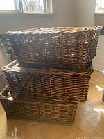 Three large wicker baskets stacked on hardwood floor showing side profile and handle placement