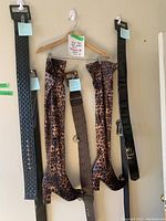 Front view of leopard print knee-high boots and four belts hanging on hooks, showing sizes and details.