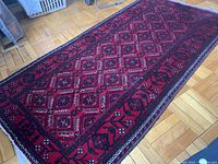Angled view of full rug on wooden floor, showing diamond pattern and border design