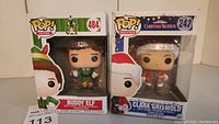 Photo showing both Buddy Elf and Clark Griswold vinyl figures in original boxes. Boxes are intact; Clark Griswold box shows visible crease.