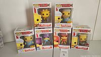 Front view of the boxed Funko Pop! figures posed together showing Homer Muumuu, Lisa Simpson, Radioactive Man, Bartman, and Gamer Bart figures.