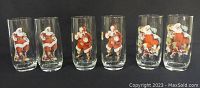 Photo showing all six Coca-Cola glasses featuring Santa Claus illustrations arranged in a row