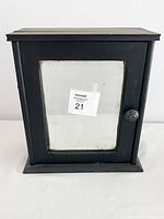 Front view of the black wood medicine cabinet with beveled glass door and round knob.