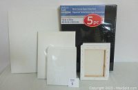 Five black 16x20 canvases in factory sealed packaging, along with the white canvases of various sizes stacked and arranged in front.