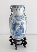 Front angle view of the blue and white ceramic vase on the wooden stand showing the bird and floral artwork.