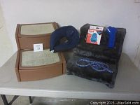 Two pet stairs, inflatable dog neck donut, poop bag dispenser and leash on white table.