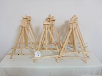 Eight wooden art easels arranged on a table, some with visible paint marks, foldable tripod design for canvases up to 16x20 inches.
