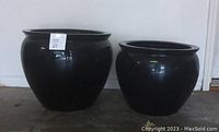 Two black fiberglass planters of different sizes shown side by side on floor.