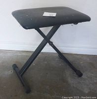 Full view of foldable cushioned bench showing black seat with some wear marks and X-style metal legs with rubber feet on floor.