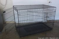 Front view of the large black wire dog crate with open door and plastic base inside.