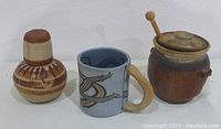 Three vintage pottery items: brown honey pot with lid and wand, blue mug with serpent handle, brown water carafe with matching cup