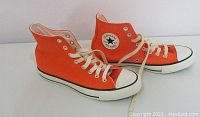 Side angle of the pair of orange Converse Chuck Taylor high tops showing the canvas, laces, and logo patch.