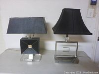 Full view of both lamps side by side showing black shades and acrylic/metal bases.