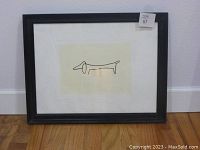 Framed art print showing the entire piece including black frame and white matte, placed on wooden floor against white wall.