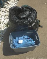 Rolled black and green pool cover tied with cords next to gray bin containing blue water tubes.