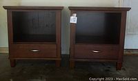 Front view of two brown wood side tables with single open shelf and drawer, metal pull handle on drawer.