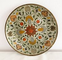 Front view of the round brass decorative plate showing colorful painted enamel floral and scroll pattern typical of the 1970s style.