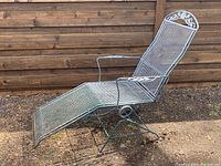 Side angle view of vintage wrought iron chaise lounge rocker showing mesh seat, reclining backrest, armrests, and decorative scrollwork.