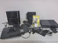 Four consoles (PS3 fat, PS3 Slim, PS2 Slim, Xbox One) arranged front view with controllers, remote and cables