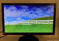 Front view of monitor displaying a green field and blue sky with clouds