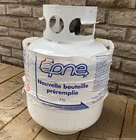 Full view of white propane tank with blue/red label in French indicating 8 kg fill weight.