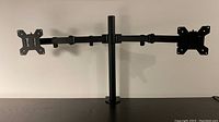 Full view of the black dual monitor desk mount stand showing two articulating arms attached to a central vertical pole with mounting clamp at the bottom.