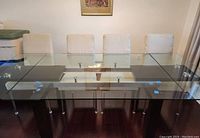 Front view of the fully extended glass dining table with beige upholstered chairs