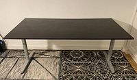 Front view of the rectangular black Ikea Galant desk with silver metal legs on a patterned rug.