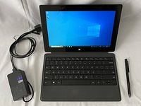 Surface Pro 2 assembled with Type Cover keyboard attached, Windows 10 Pro screen on, power adapter and cable visible