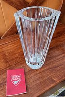 Clear Orrefors solid crystal vase shown on wooden surface with Orrefors Sweden booklet or tag next to it, front angled view revealing vertical faceted designs and polished thick base.