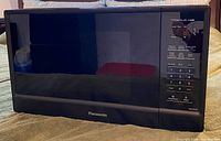 Front view of Panasonic black microwave oven showing entire unit and front door with Panasonic logo.