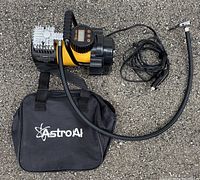 Top view of the portable air compressor, showing yellow and black body, attached hose, power cord, and black AstroAI carrying bag.