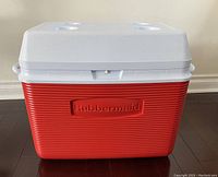 Front view of the cooler showing red body, white lid with cup holders, and Rubbermaid embossed logo.
