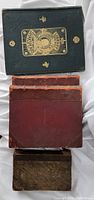 Stack of four vintage hardcover books showing covers and condition: green embossed Shakespeare book, two red-brown leather books, and one mottled dark cover book