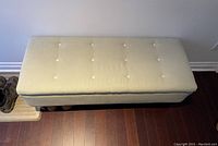 Top view of a rectangular light green upholstered storage ottoman with eight cream-colored buttons tufted on the lid.