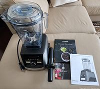 Motor base, blending container with lid, tamper and printed materials on sofa